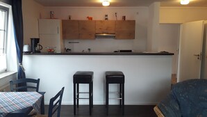 A compact kitchen with two stools, a dining table with a checkered tablecloth, and a sofa. - Pension Norddeicher Straße (Norden)