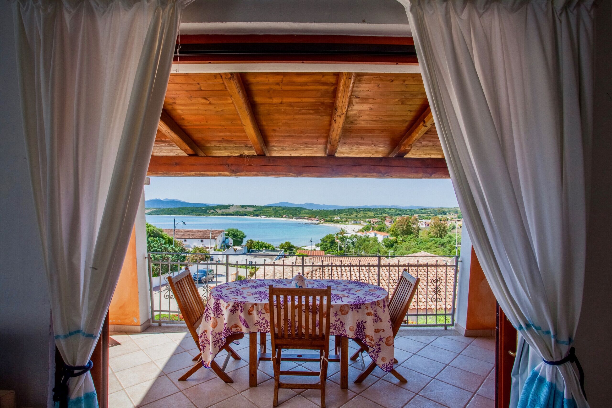 A balcony with a table and chairs, overlooking a scenic view of the sea and landscape.