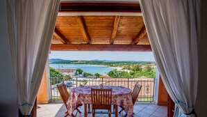 A balcony with a table and chairs, overlooking a scenic view of the sea and landscape.