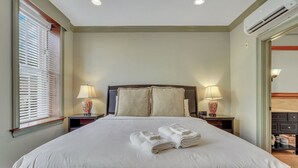 Un lit bien fait, avec des serviettes pliées, une table de chevet avec une lampe et une petite table à côté du lit ornée d’un vase.