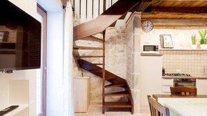 Una cocina con pared de piedra, escalera de madera y un reloj en la pared.