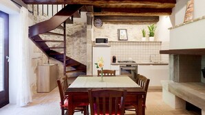 Una cocina rústica con pared de piedra, escalera de madera y un comedor con mesa y sillas.