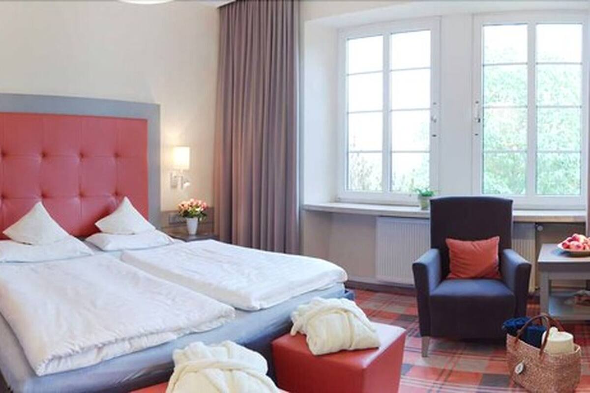 Une chambre d’hôtel avec un grand lit, une chaise, une petite table et une fenêtre donnant sur un paysage verdoyant.