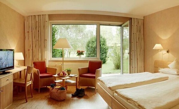 Une chambre d’hôtel avec un lit, deux chaises, une petite table, un téléviseur et une fenêtre avec des rideaux.