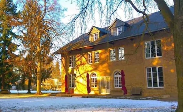 Un edificio de dos pisos con fachada simétrica, ventanas grandes y suelo cubierto de nieve.