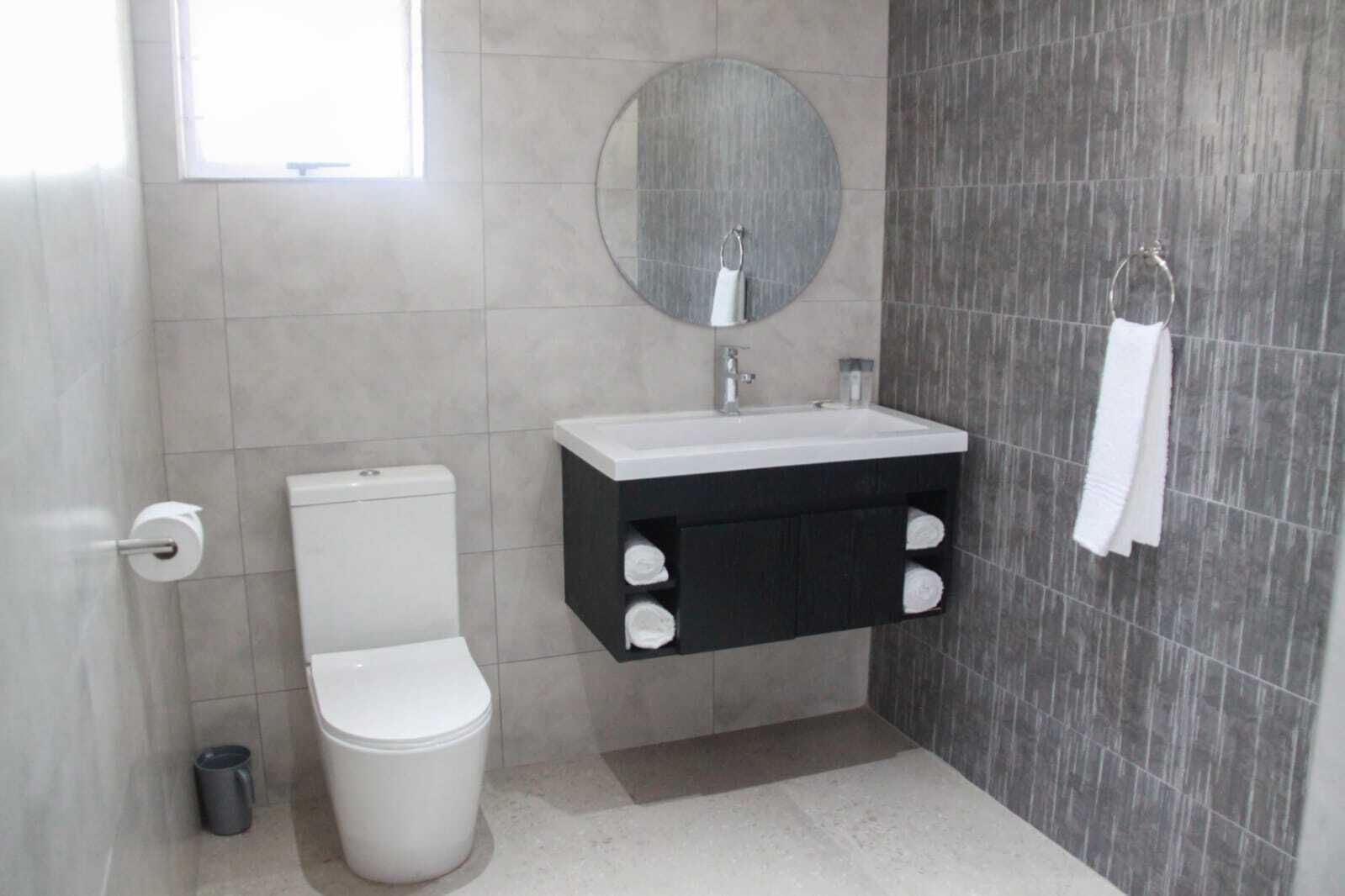 Ein Badezimmer mit Toilette, Waschbecken mit Spiegel darüber und einem Handtuch an der Wand.