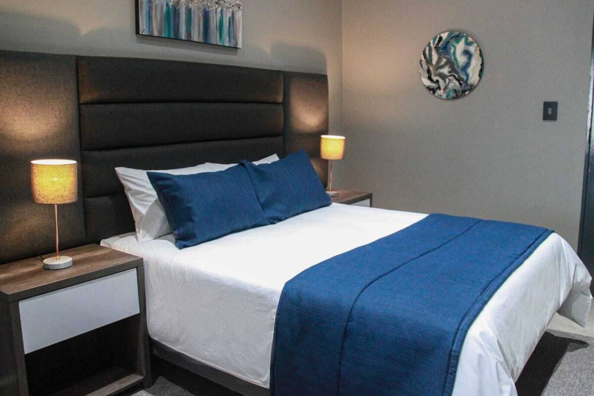 A neatly made bed with a blue blanket and pillows, flanked by two bedside lamps on wooden nightstands.