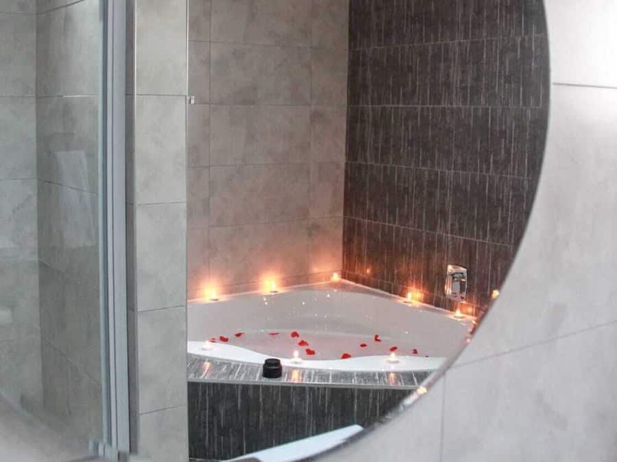 Un bagno moderno con uno specchio grande, una vasca da bagno con petali di rosa e un angolo doccia.