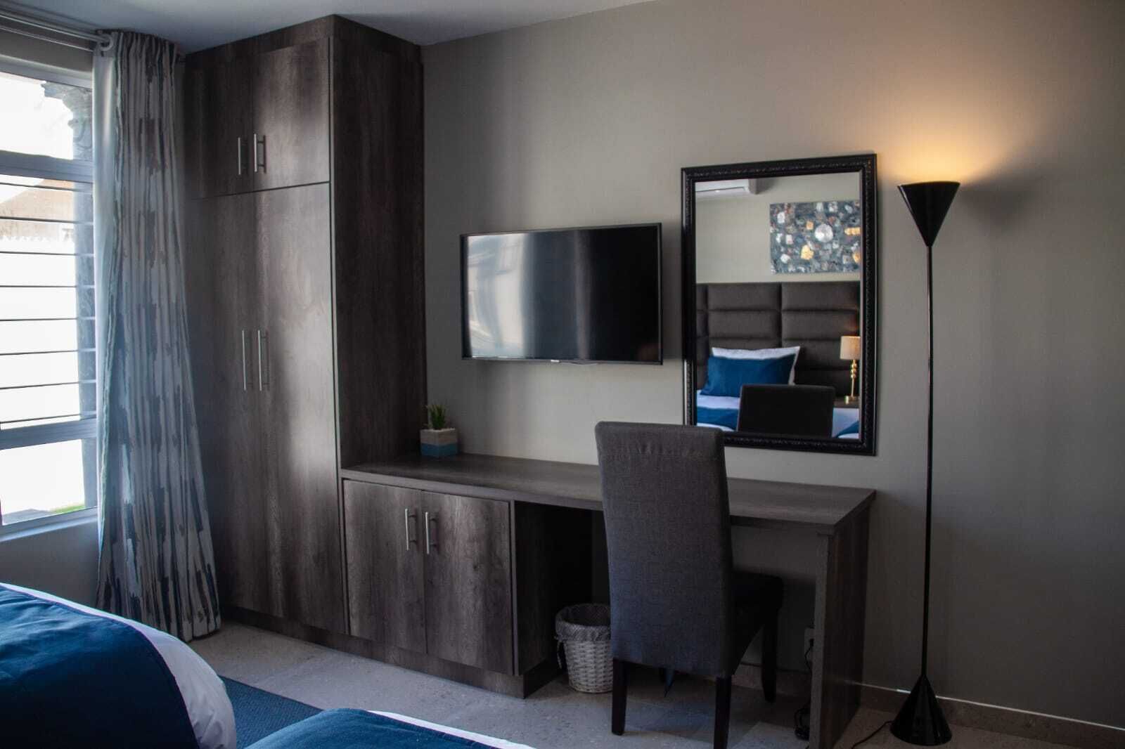 Un dormitorio moderno con cama, escritorio, silla, televisor, espejo y lámpara de pie.