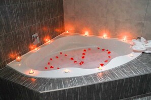 A large, oval-shaped bathtub with candles and rose petals, surrounded by dark, textured walls. - The Cato Suites Hotel (Durban)