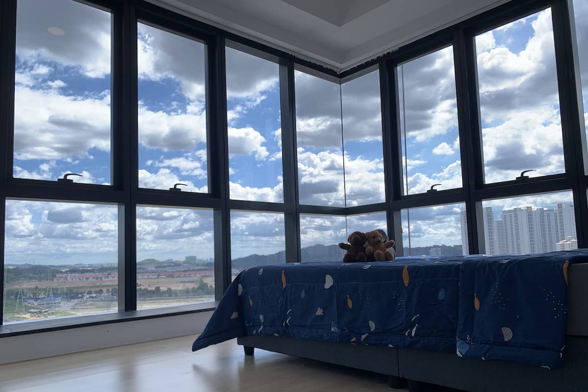 Ein Zimmer mit großen Fenstern, einem Bett und einem Teddybären.