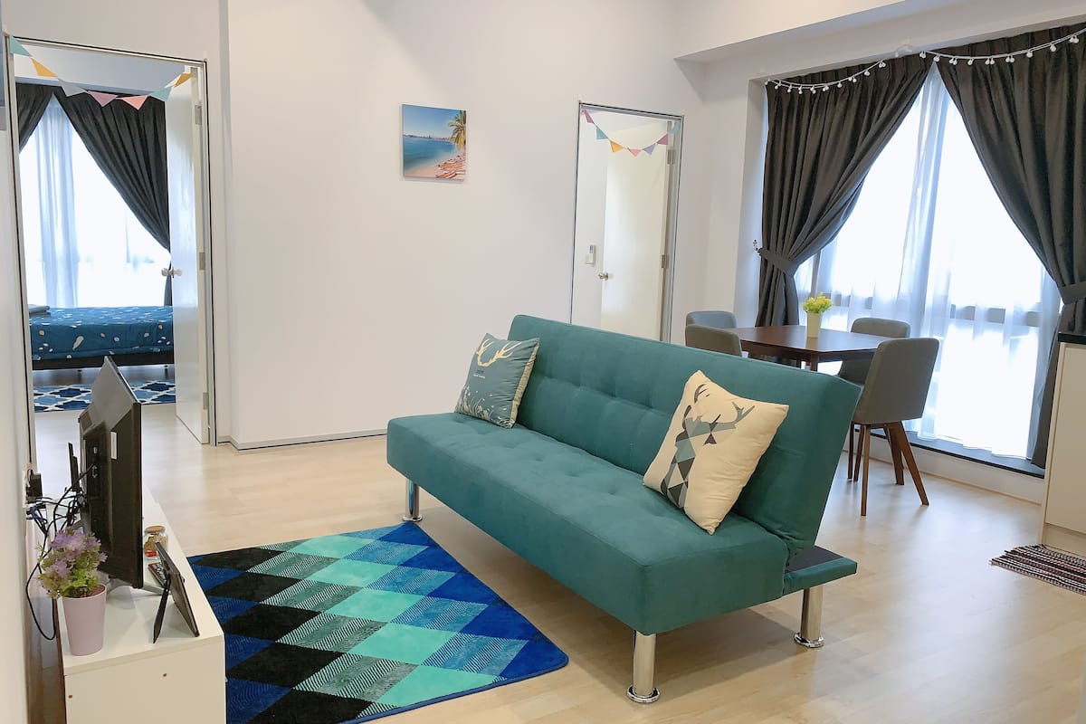 Ein modernes Wohnzimmer mit einem türkisfarbenen Sofa, einem gemusterten Teppich und einem Essbereich mit Tisch und Stühlen.