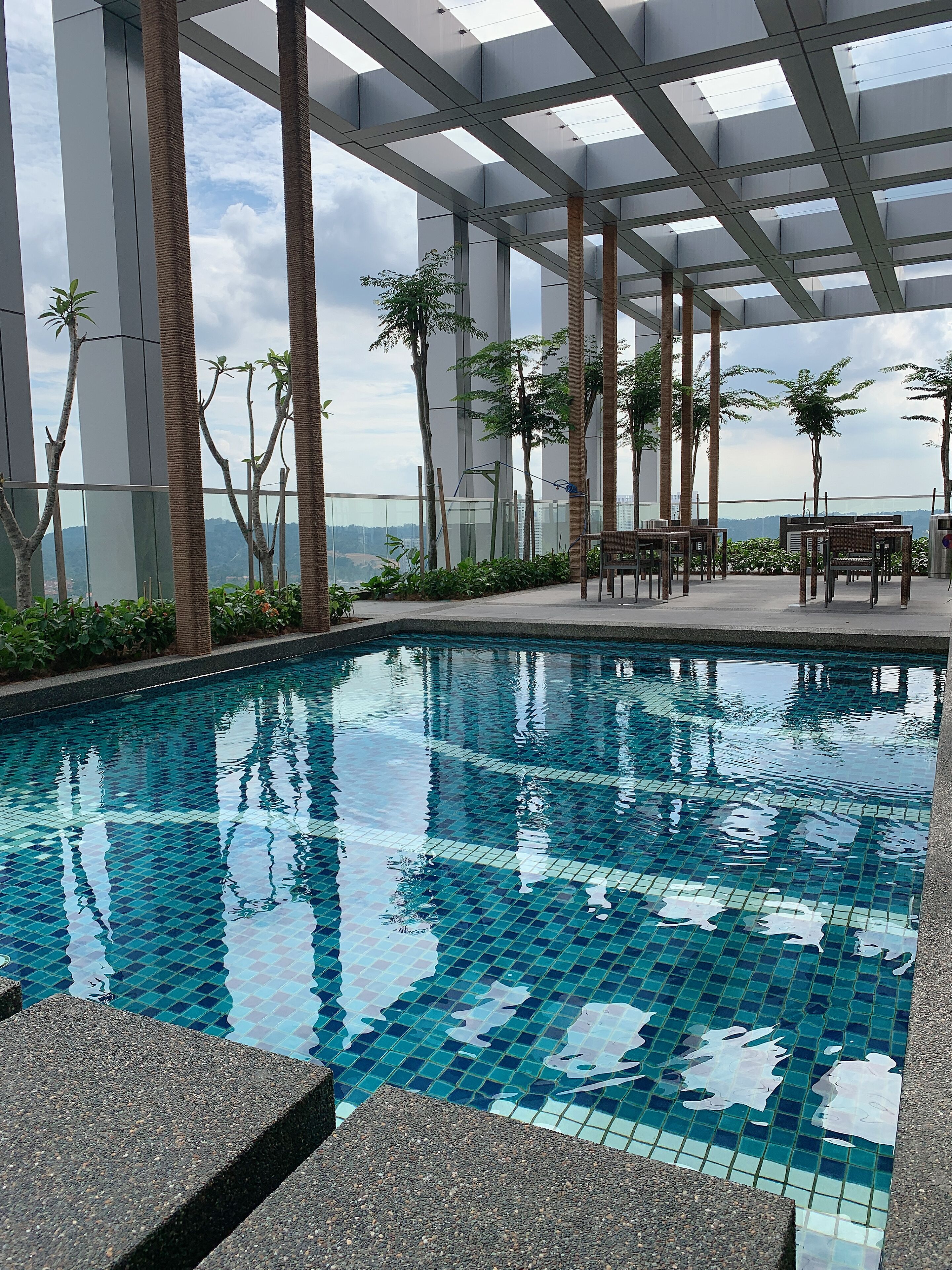An indoor swimming pool with tiled flooring, surrounded by tall columns and potted plants.