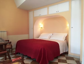 A bedroom with a bed, a red blanket, a wooden table with chairs, and a radiator.
