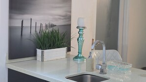 Eine Küchenarbeitsplatte mit Spüle, einem türkisfarbenen Kerzenhalter, einem Blumentopf und einem gerahmten Bild von einer Strandlandschaft.