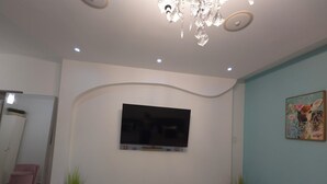 Ein modernes Wohnzimmer mit einem an der Wand befestigten Flachbildfernseher, einer kleinen Digitaluhr und zwei Zimmerpflanzen.