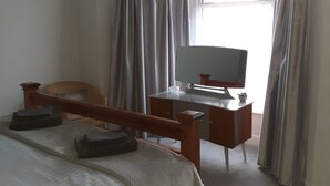A bedroom with a bed, a desk, a chair, a television, and a window with curtains. - Family holiday home near both sea front and town (Yarmouth)