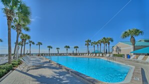 Área de piscina com espreguiçadeiras e palmeiras, sob um céu azul límpido.