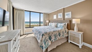 Quarto com cama grande, televisão, mesa de cabeceira e vista para a praia.