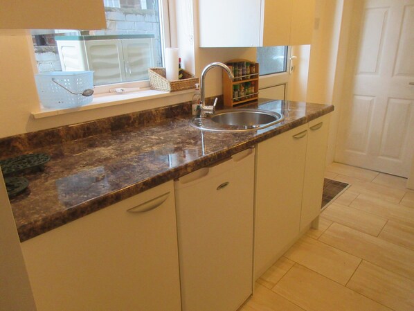 Kitchen area with granite countertop, stainless steel sink, and white cabinetry.