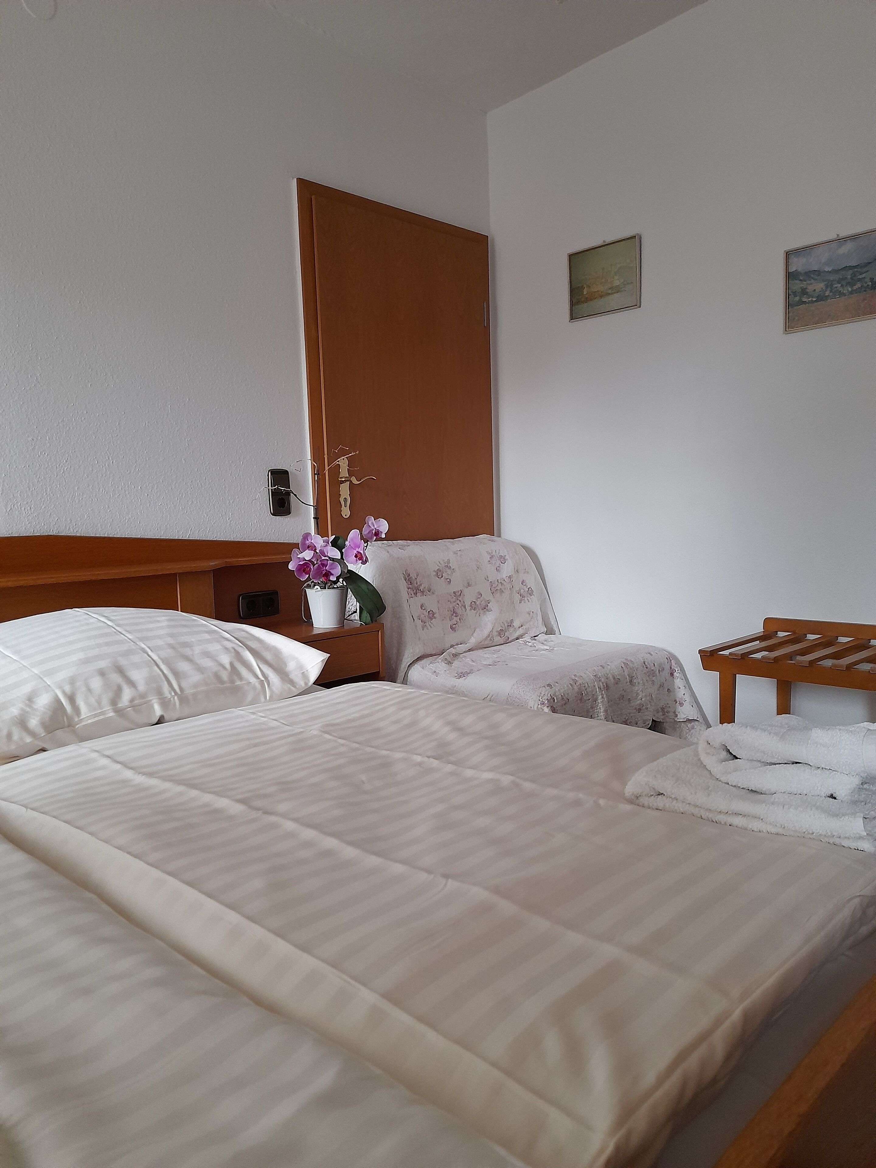 A hotel room with two beds, a wooden headboard, a nightstand with a vase of flowers, and a small table with a towel.
