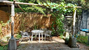 A garden patio with a round table and two chairs, surrounded by a wooden fence and greenery. - Haus Barnabas im Engel - Gasthaus Engel (Utzenfeld)
