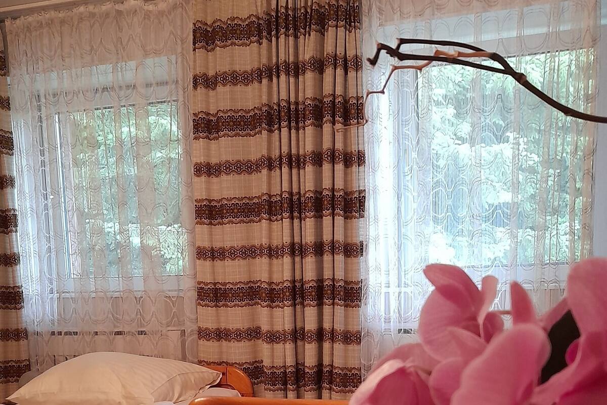 Ein Zimmer mit einem Bett, einem Holztisch und einem Fenster mit Vorhängen.