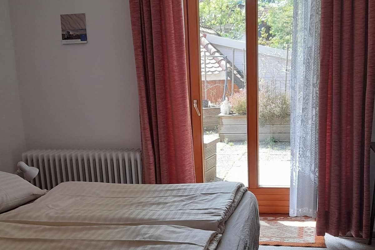 Ein Schlafzimmer mit Bett, Heizkörper, blauem Teppich und Blick nach draußen.