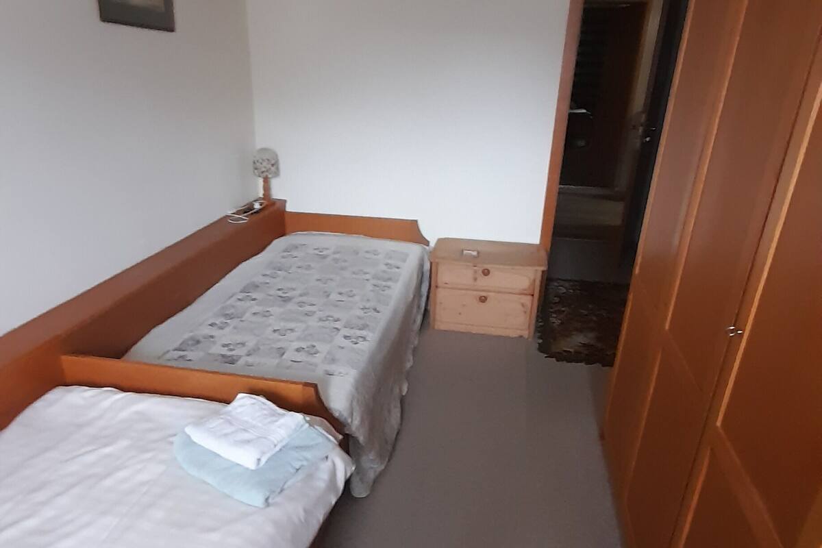 Ein kleiner, schmaler Raum mit zwei Einzelbetten, einem Holzschrank, einer kleinen Holzeinrichtung und einer Pendelleuchte.
