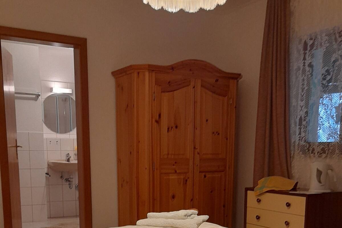 Ein Schlafzimmer mit einem großen Bett, einem Holzschrank und einem durchgehenden Türrahmen einsehbaren Badezimmer.