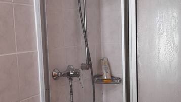 A glass-enclosed shower with a handheld showerhead and a handheld faucet.