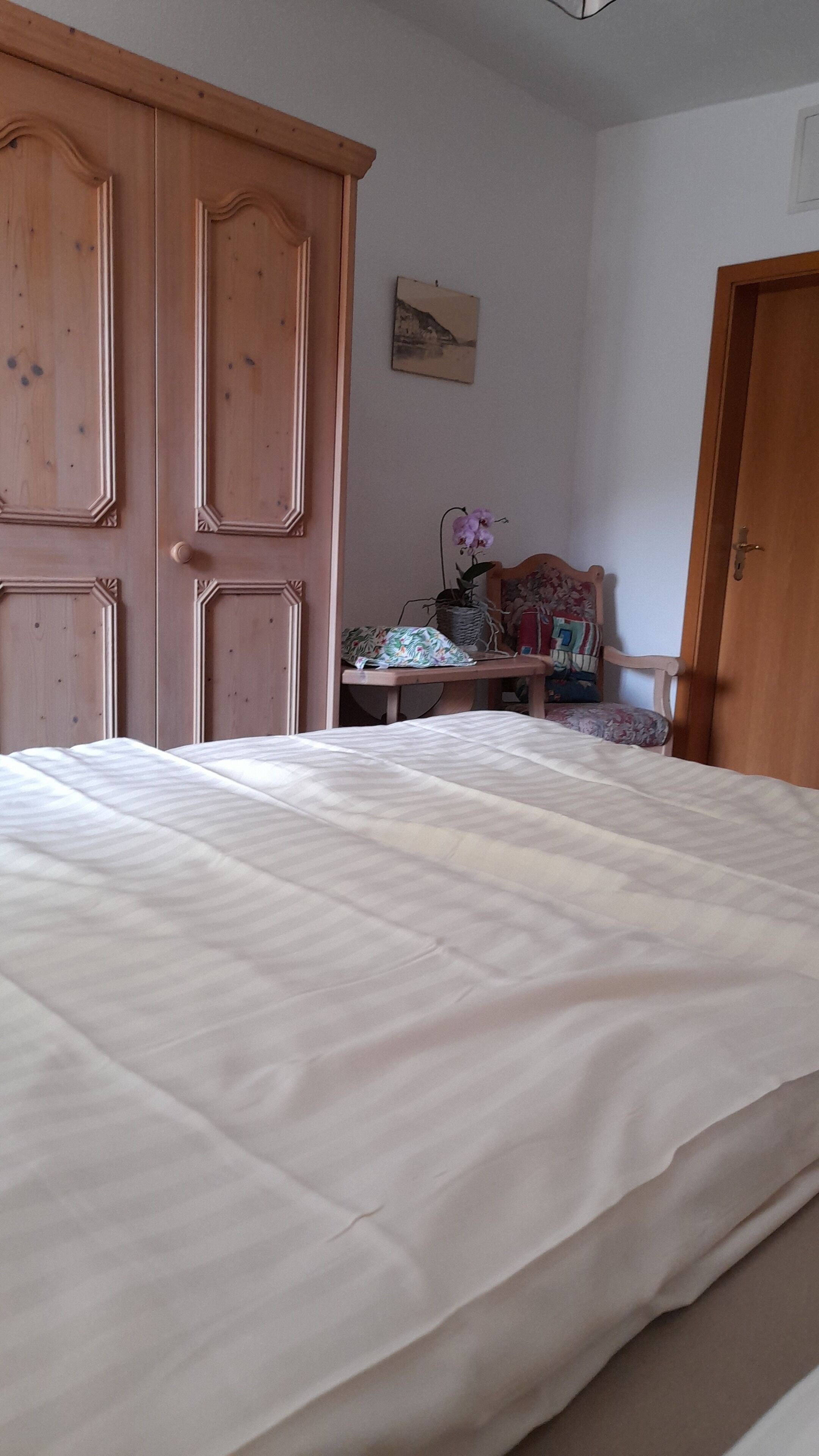 A bedroom with a large bed, wooden wardrobe, and a small table with a plant.