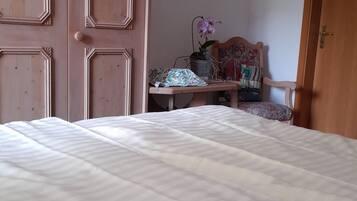 A bedroom with a large bed, wooden wardrobe, and a small table with a plant.