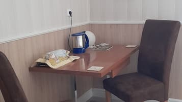 Un comedor con una mesa de madera, dos sillas marrones, un hervidor azul y un adorno rojo en la pared.