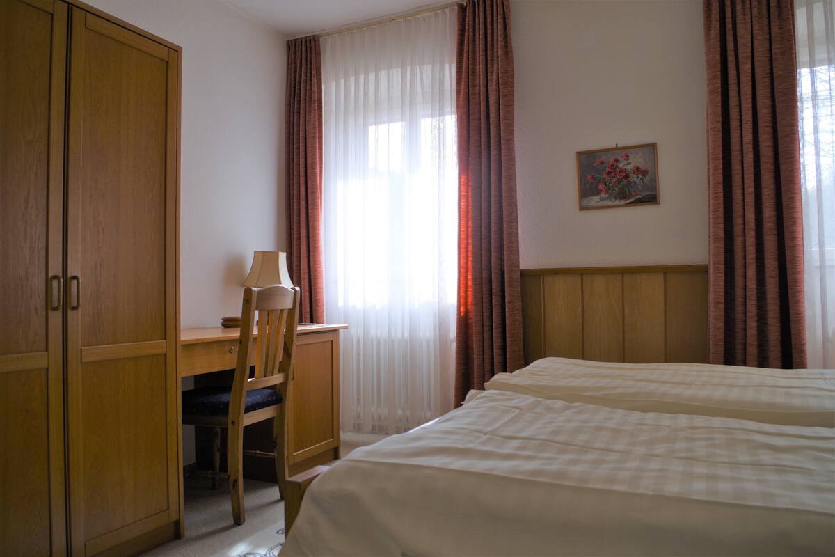 Ein Hotelzimmer mit zwei Betten, einem Schreibtisch mit Stuhl, einem Kleiderschrank und einem Bild an der Wand.