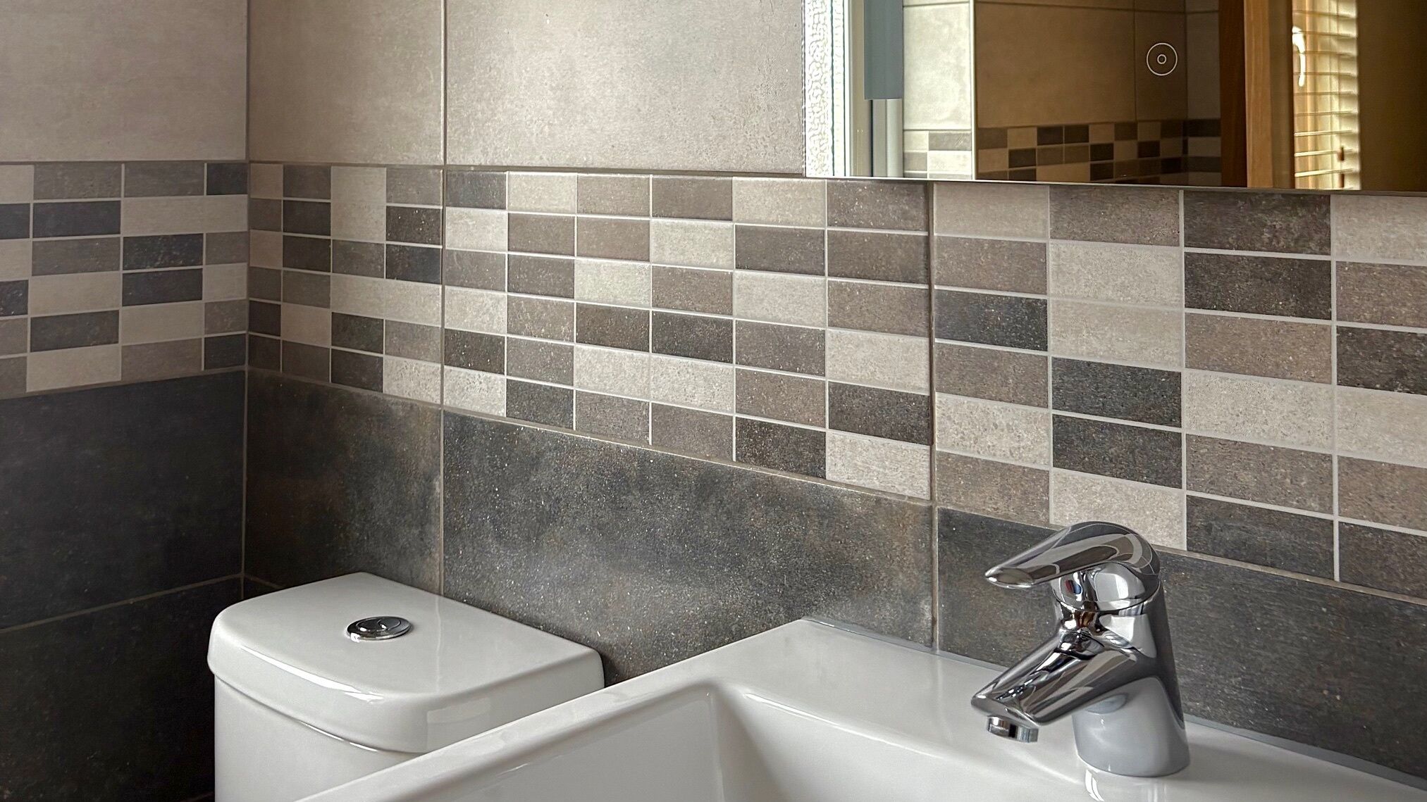 Un baño con inodoro y lavamanos blancos, grifo cromado y salpicadero de azulejos con diseño a cuadros.