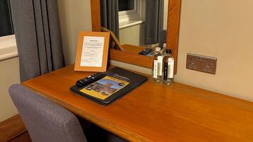 A hotel room desk with a framed general enquiries sign, a remote control, a brochure, and two bottles of water.