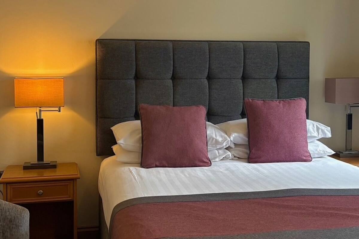 A hotel room with a large bed, two pillows, a bedside lamp, and a nightstand.