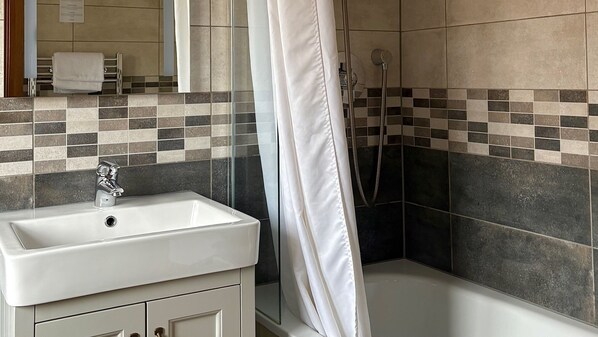 Une salle de bain avec un lavabo blanc, une douche avec un rideau et des murs carrelés.