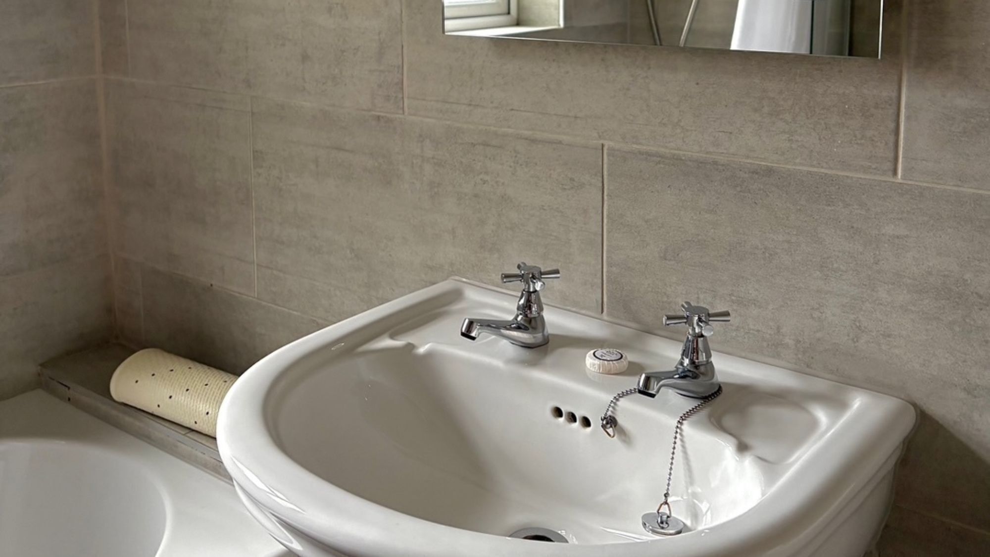 A bathroom with a white sink, two faucets, and a toilet with a beige toilet paper holder.