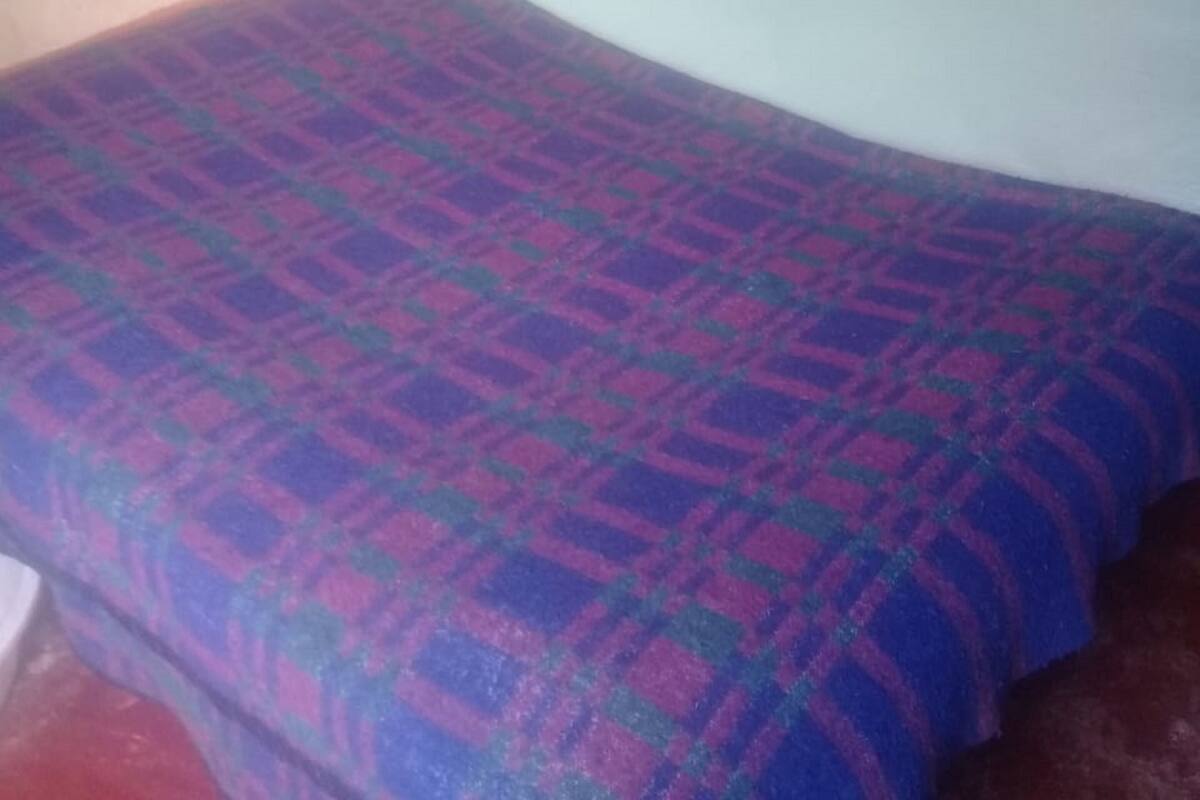 A single bed with a patterned bedspread in a room with plain walls and a visible wooden headboard.