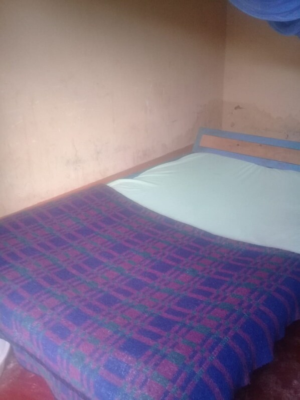 A single bed with a patterned bedspread in a room with plain walls and a visible wooden headboard.