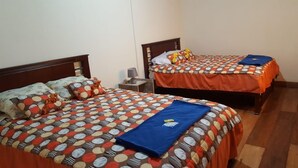 Two single beds with matching headboards and footboards, a nightstand with a lamp, and a blue towel on the floor. - El Aguacate (Baños de Agua Santa)