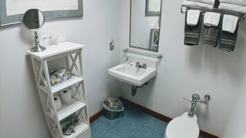 Et badeværelse med hvid vask, spejl, toilet og et hyldesæt med toiletartikler.
