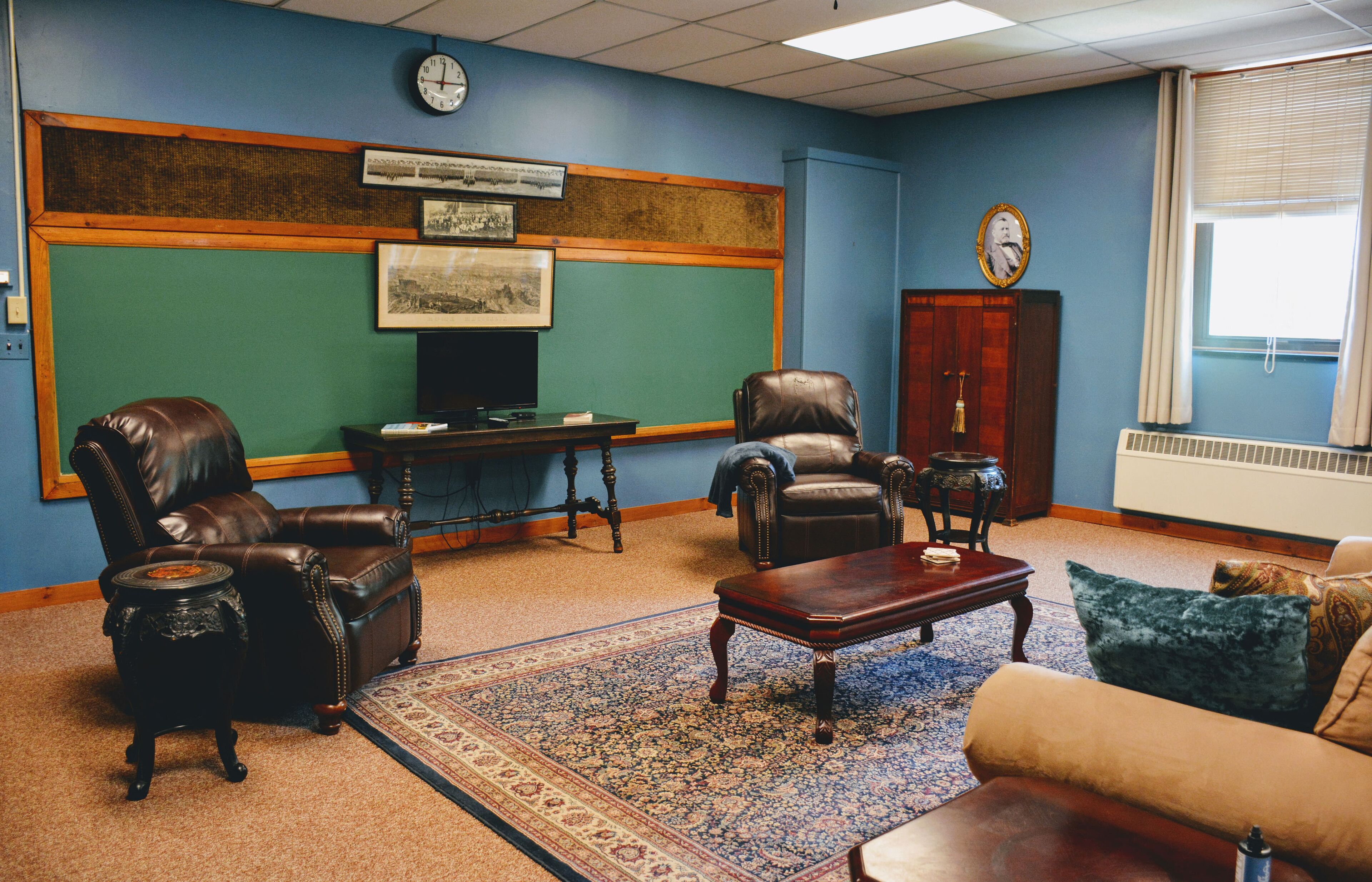 A room with a green chalkboard wall, two leather armchairs, a wooden coffee table, and a blue patterned rug.
