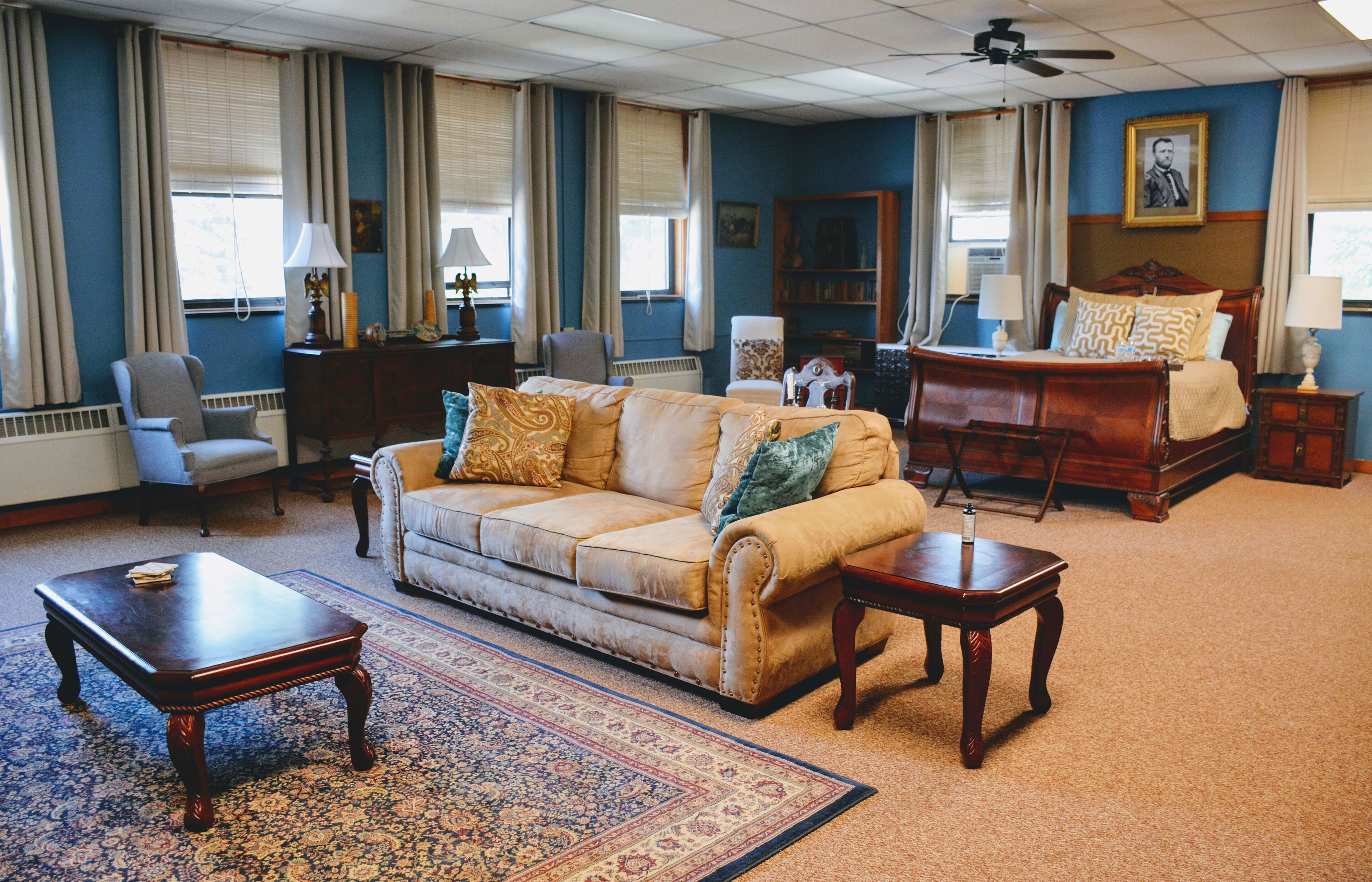 Een ruime woonkamer met een grote bank, een salontafel en een open haard. Er staan twee fauteuils en een boekenkast in de kamer.