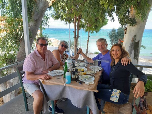 A group of people dining at an outdoor table with a view of the sea.