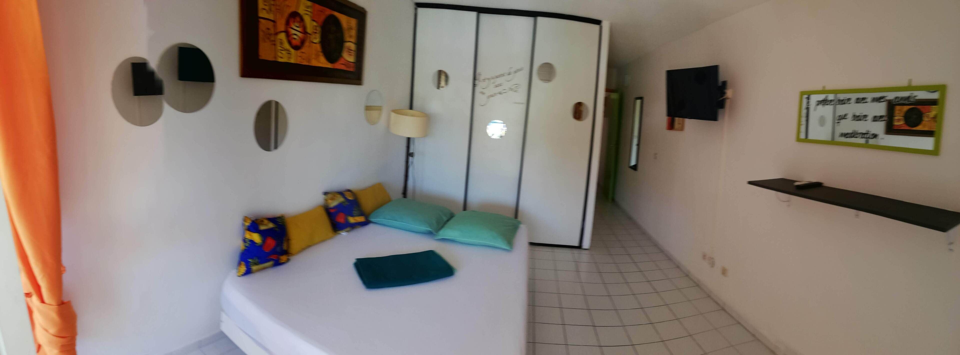 Un dormitorio con cama, almohadas, un armario, un espejo, una lámpara y una estantería.