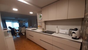 A modern kitchen with white cabinets, a black countertop, and a coffee machine. - Sunset on the beach, Salou (Tarragona)