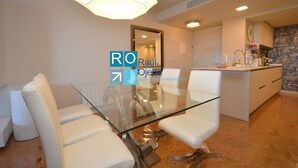 A modern kitchen with a stone backsplash, a glass dining table with white chairs, and a pendant light. - Sunset on the beach, Salou (Tarragona)